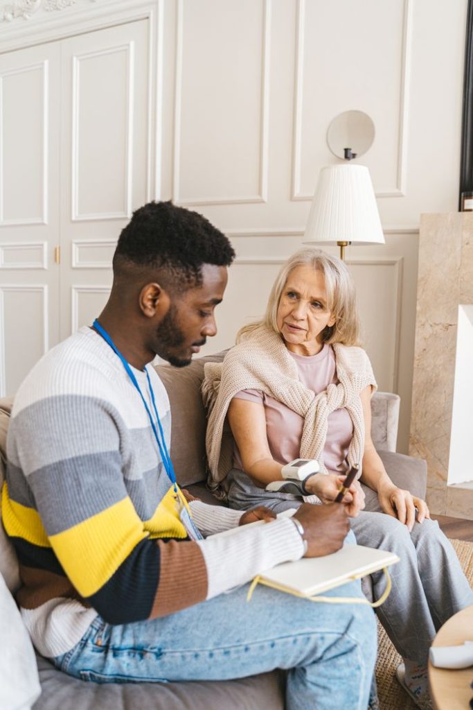 A caring volunteer assists an elderly woman in monitoring her blood pressure indoors.